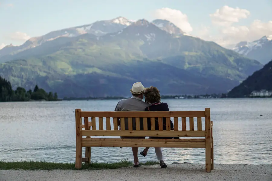 Älteres Paar auf einer Bank am See mit Blick auf die Berge